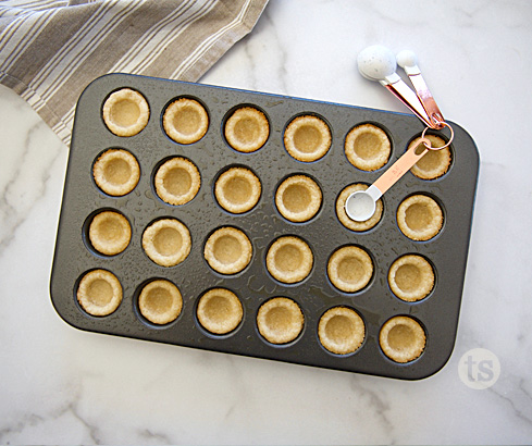 overhead of baked cookie cups, showing the measuring teaspoon pushing one down