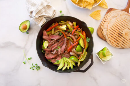 Steak, veggies avocados, limes in cast iron pan